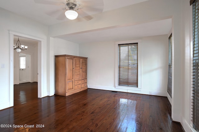 empty room with ceiling fan with notable chandelier, dark wood-type flooring, and a wealth of natural light