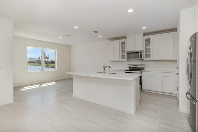 kitchen featuring appliances with stainless steel finishes, sink, light tile patterned floors, a center island with sink, and white cabinetry