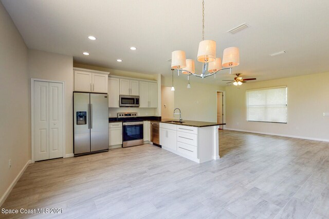 kitchen featuring decorative light fixtures, stainless steel appliances, white cabinets, sink, and light hardwood / wood-style floors