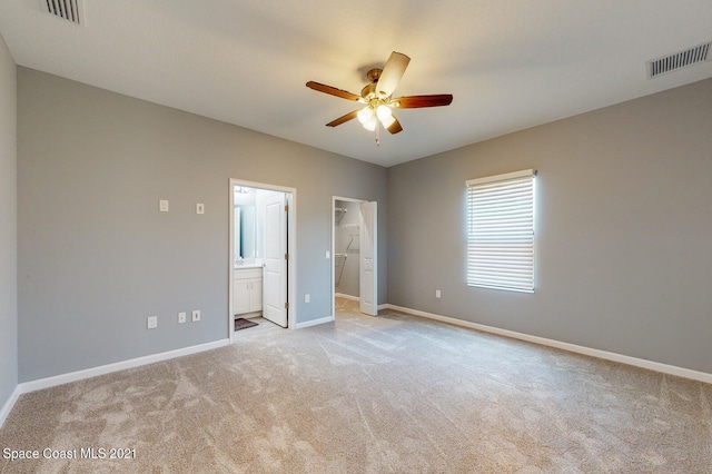 unfurnished bedroom featuring ceiling fan, a walk in closet, light carpet, and connected bathroom