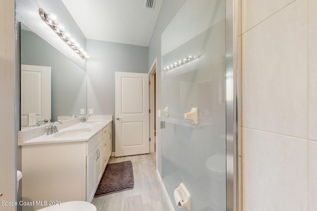 bathroom featuring hardwood / wood-style flooring, a shower with door, toilet, and dual bowl vanity