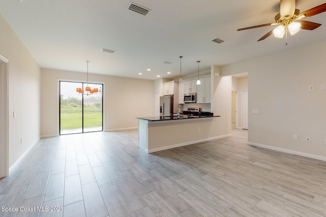 kitchen with appliances with stainless steel finishes, pendant lighting, ceiling fan with notable chandelier, and white cabinets