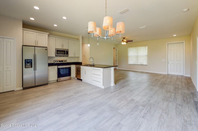 kitchen with appliances with stainless steel finishes, sink, hanging light fixtures, light hardwood / wood-style floors, and white cabinetry