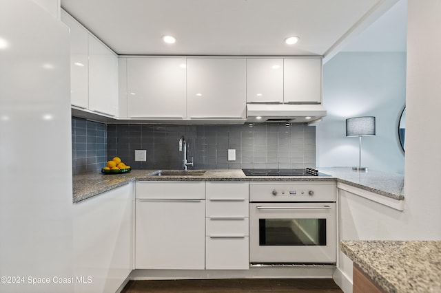 kitchen featuring dark hardwood / wood-style flooring, light stone counters, sink, white cabinets, and oven