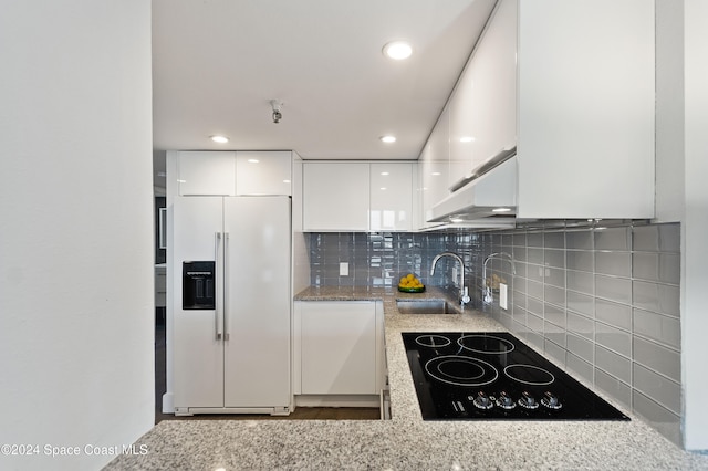 kitchen featuring white refrigerator with ice dispenser, sink, decorative backsplash, black electric cooktop, and white cabinetry