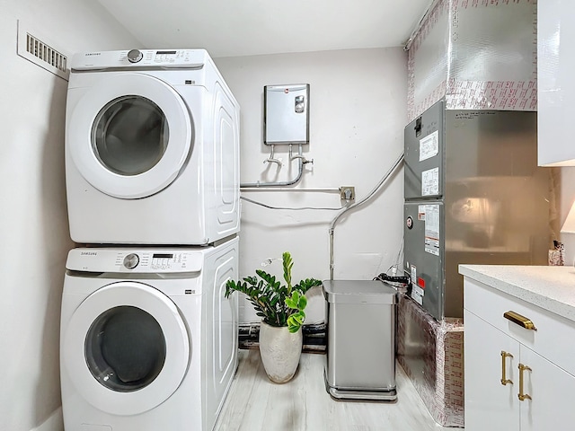 laundry area with cabinets, light wood-type flooring, and stacked washer and clothes dryer