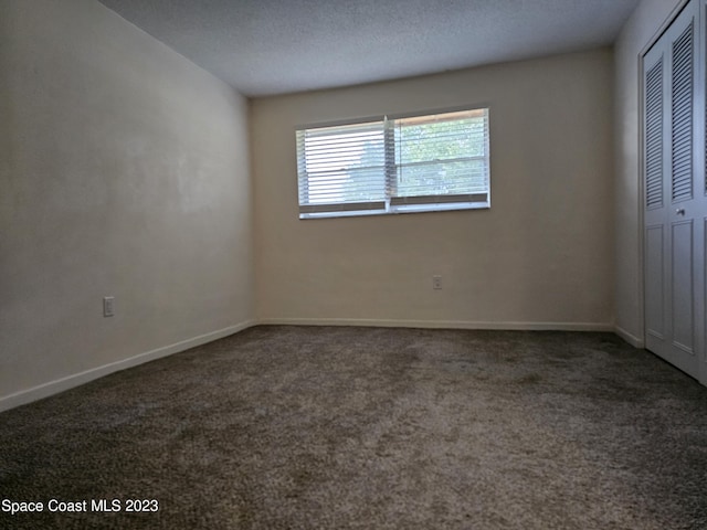 unfurnished bedroom with dark colored carpet, a textured ceiling, and a closet