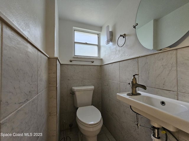 bathroom featuring toilet, sink, and tile walls