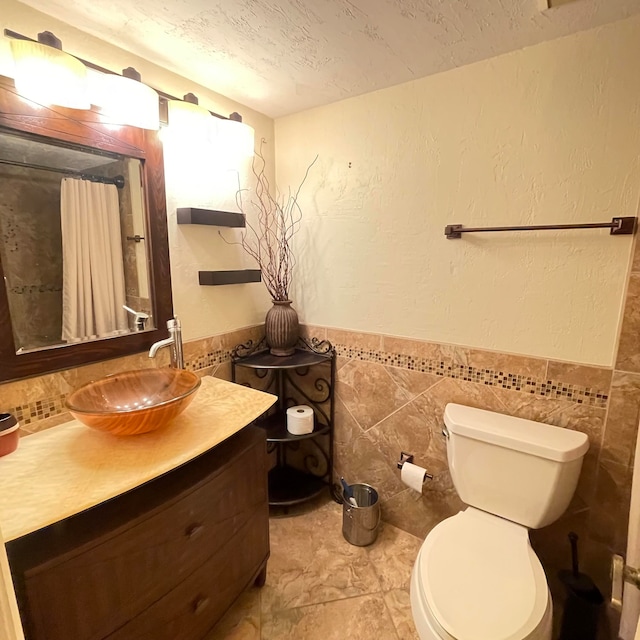 bathroom with vanity, tile patterned floors, tile walls, toilet, and a textured ceiling