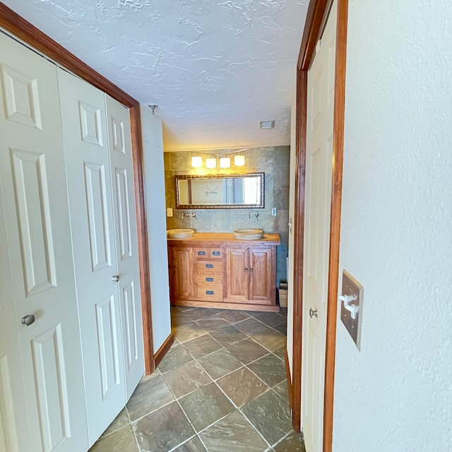 interior space featuring tile patterned floors, a textured ceiling, and dual bowl vanity