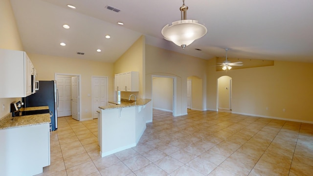 kitchen with high vaulted ceiling, kitchen peninsula, ceiling fan, light stone countertops, and white cabinetry