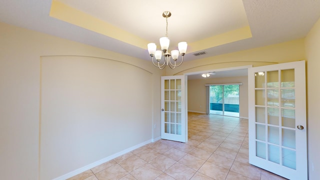 unfurnished dining area with a raised ceiling, french doors, light tile patterned floors, and a chandelier