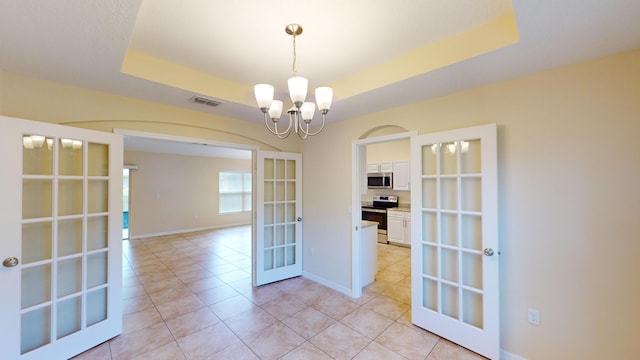 unfurnished dining area featuring an inviting chandelier, french doors, light tile patterned floors, and a tray ceiling