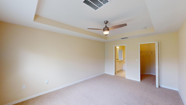 unfurnished bedroom featuring a tray ceiling, a walk in closet, ceiling fan, and a closet