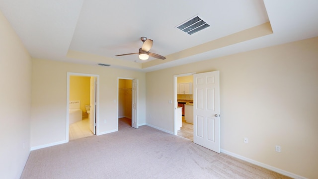 unfurnished bedroom featuring a raised ceiling, a spacious closet, connected bathroom, and a closet