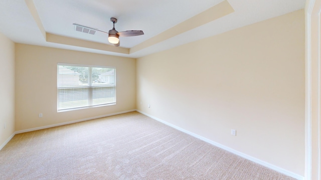 empty room with a tray ceiling, ceiling fan, and light colored carpet