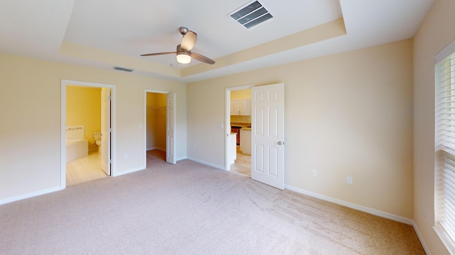 unfurnished bedroom featuring a raised ceiling, ceiling fan, a spacious closet, connected bathroom, and a closet