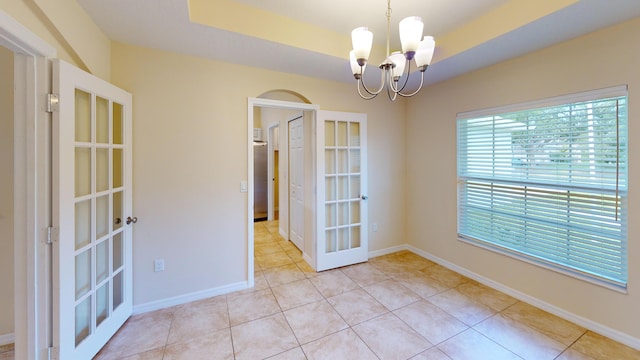 empty room featuring a tray ceiling, french doors, light tile patterned floors, and a chandelier