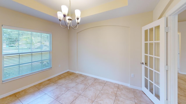 tiled spare room featuring a tray ceiling and an inviting chandelier