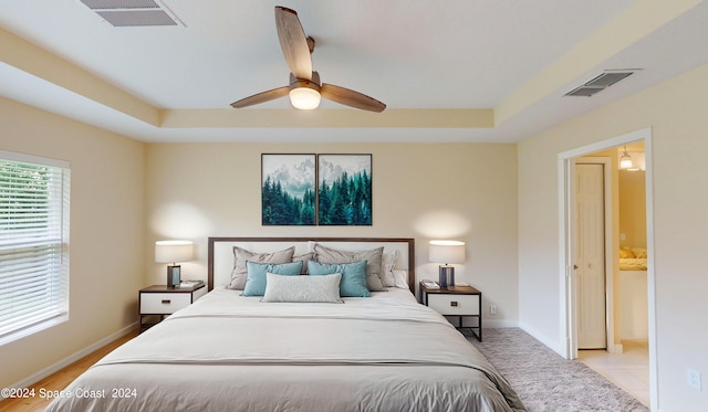 bedroom featuring ceiling fan, ensuite bathroom, and a tray ceiling