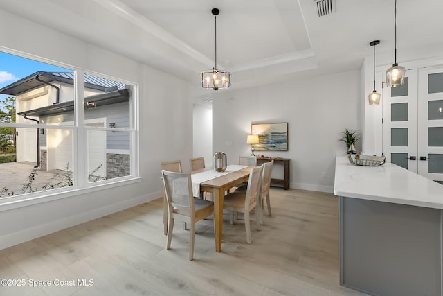 dining space with light hardwood / wood-style floors, a raised ceiling, and a healthy amount of sunlight