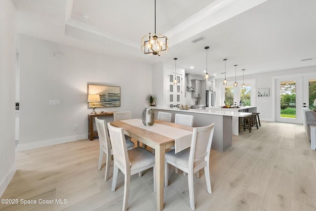 dining area featuring a raised ceiling, light wood-type flooring, french doors, and a chandelier