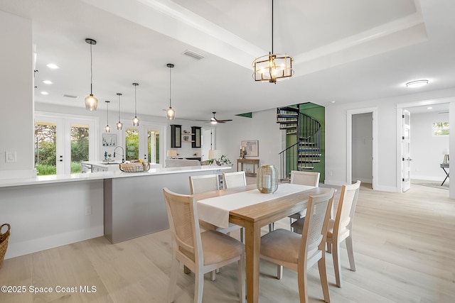 dining area with ceiling fan, a tray ceiling, french doors, light hardwood / wood-style flooring, and sink