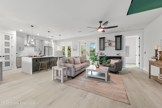 living room with light wood-type flooring, french doors, sink, and ceiling fan