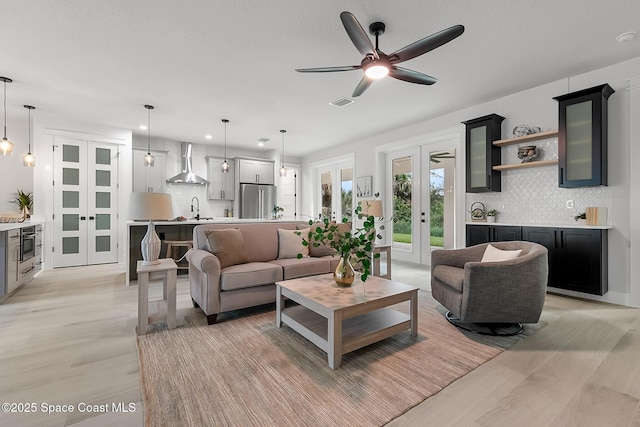 living room with ceiling fan, french doors, sink, and light hardwood / wood-style floors