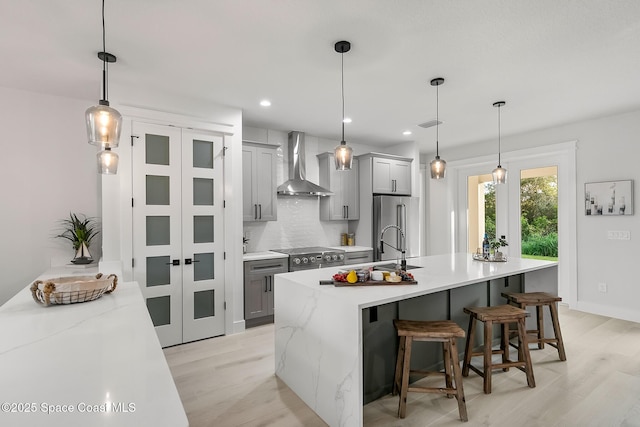 kitchen featuring gray cabinetry, a center island with sink, and wall chimney range hood