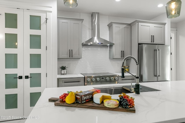 kitchen with wall chimney exhaust hood, decorative backsplash, light stone counters, gray cabinetry, and high end fridge