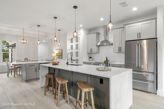 kitchen featuring pendant lighting, sink, appliances with stainless steel finishes, an island with sink, and wall chimney exhaust hood