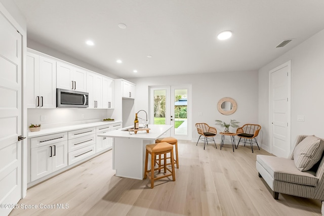 kitchen featuring white cabinets, a breakfast bar, an island with sink, and light hardwood / wood-style flooring