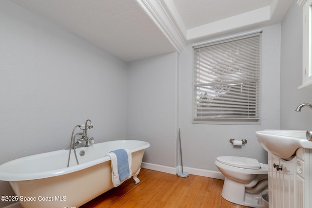 bathroom featuring hardwood / wood-style floors, vanity, toilet, a tub to relax in, and a textured ceiling