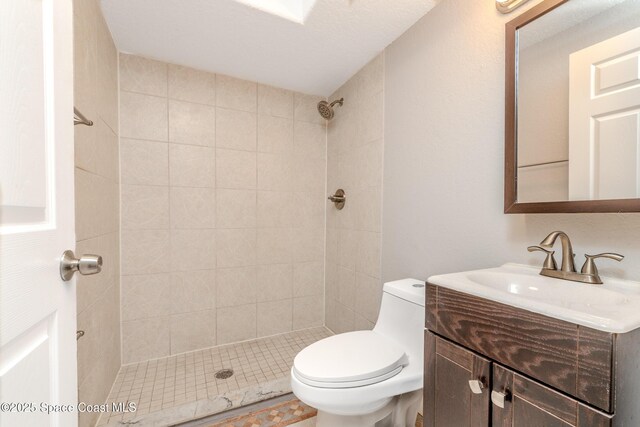 bathroom with tiled shower, vanity, and toilet