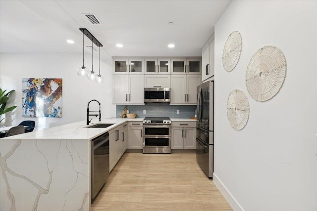 kitchen featuring kitchen peninsula, appliances with stainless steel finishes, sink, white cabinets, and hanging light fixtures