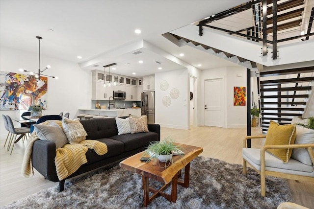 living room featuring sink, light hardwood / wood-style flooring, and an inviting chandelier