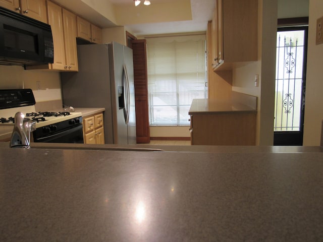 kitchen with light brown cabinets, white gas range oven, a raised ceiling, and plenty of natural light