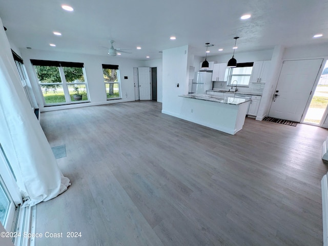 kitchen with light wood-type flooring, backsplash, white refrigerator, decorative light fixtures, and white cabinetry