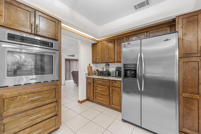 kitchen with appliances with stainless steel finishes, light tile patterned floors, and light stone counters