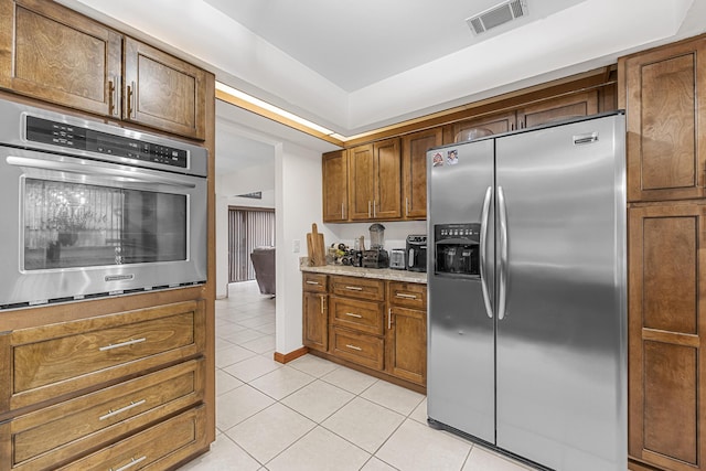 kitchen with light tile patterned floors, visible vents, baseboards, appliances with stainless steel finishes, and brown cabinets