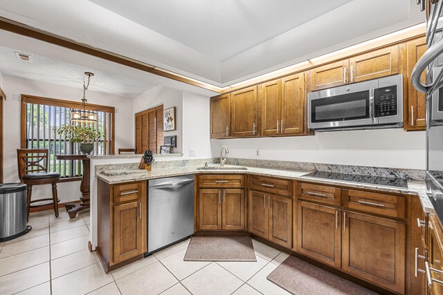 kitchen featuring a peninsula, appliances with stainless steel finishes, brown cabinetry, and a sink