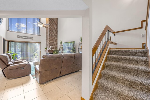 living room with a towering ceiling, brick wall, ceiling fan, and light tile patterned floors