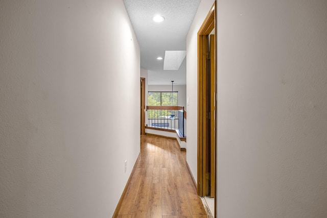 hall featuring recessed lighting, light wood-style flooring, and a textured ceiling