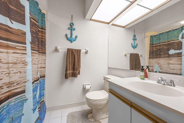 bathroom with a skylight, toilet, vanity, tile patterned flooring, and baseboards