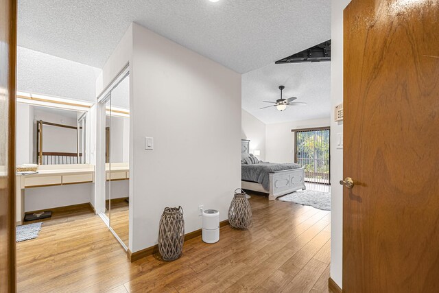 hall featuring lofted ceiling, light hardwood / wood-style flooring, and a textured ceiling