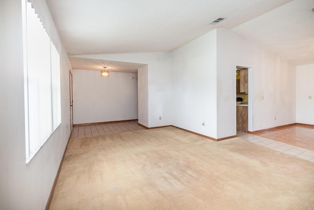 unfurnished room featuring a textured ceiling, light tile patterned floors, and lofted ceiling