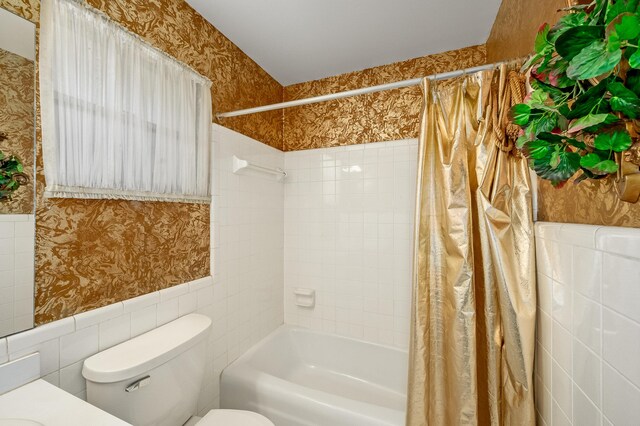 bathroom with a wainscoted wall, toilet, shower / bath combo, tile walls, and wallpapered walls