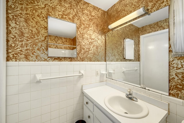 bathroom featuring wallpapered walls, vanity, a wainscoted wall, and a tile shower