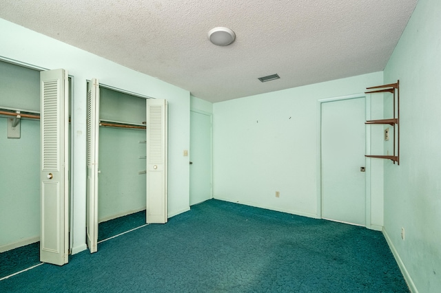 unfurnished bedroom featuring two closets, dark colored carpet, and a textured ceiling